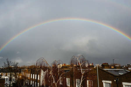 A bright rainbow brightens a grey sky over the the rooftops of Londonの写真素材