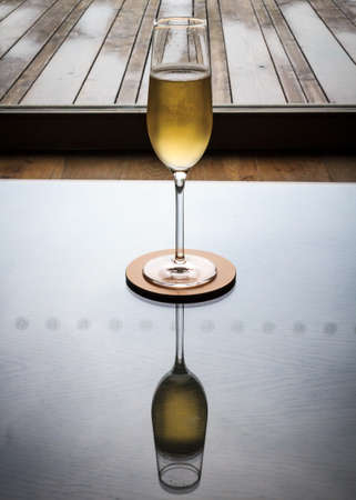 A single Champagne glass sits on a highly polished table, which shows the reflection の写真素材