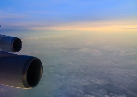 The sun and clouds create rainbow colours over the clouds, taken from a plane, with the engines and...