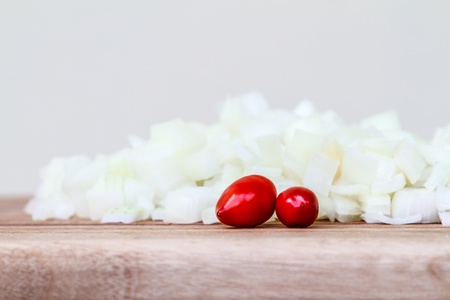 Side view of freshly chopped white onion, garnished with two fresh red chillies, on a wooden chopping boardの写真素材