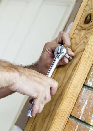 Man using a ratchet to bolt wood to a brick wall