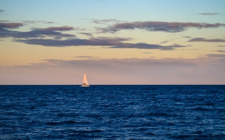 A luxury sailboat sailing on a blue ocean at twilight, catching the last purple light of dusk の写真素材
