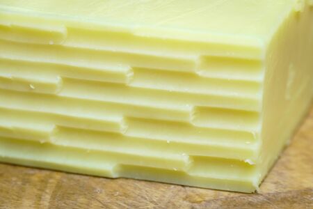 Close up of the corner of a block of cheddar cheese which has been grated, on a wooden cutting boardの写真素材