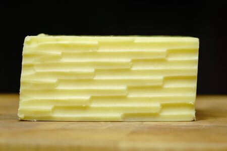 Straight on look at a block of cheddar cheese with a lined pattern from a grater, on a wooden cutting board.の写真素材