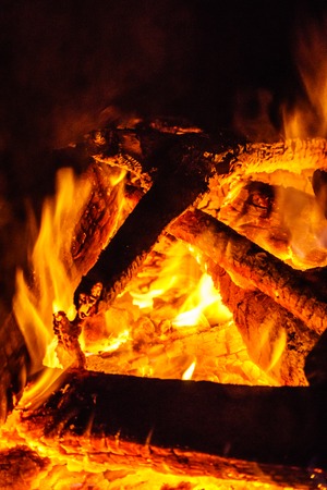 Red hot coals and flames at the base of a burning wood fire.