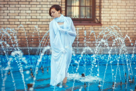 Beautiful girl in white dress standing in a fountainの写真素材