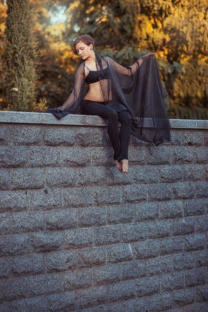 Young girl dancer in black clothes sits on a stone wall, she threw a black shawl over her shouldersの写真素材
