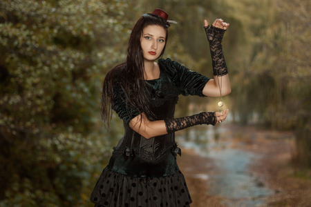 Brunette girl in black dress of gothic style holding a watch on a chainの写真素材