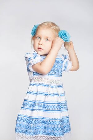 Little cute blond girl tying her hair in a tail on a white backgroundの写真素材