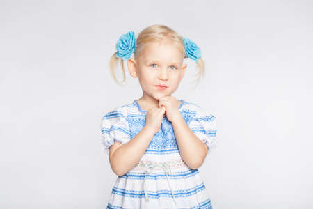 Little blond girl on a white background standing with folded handsの写真素材