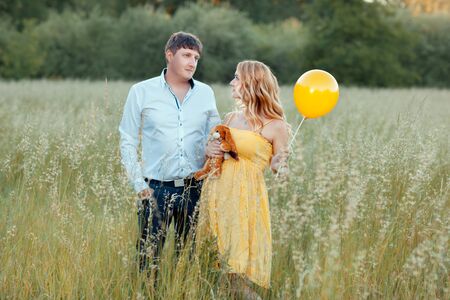 Pregnant woman standing in a field with her husband. The girl is holding a toy and a balloonの写真素材
