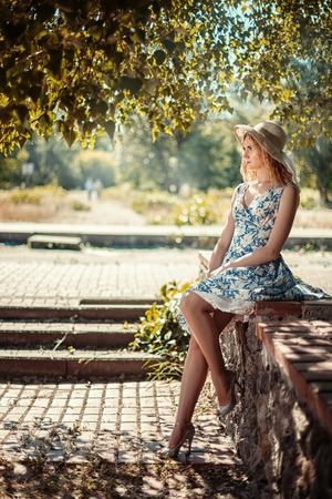Beautiful girl sitting on a stone parapet in the park and misses.の写真素材