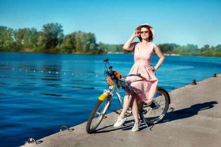 Beautiful girl in a hat and sunglasses on a bicycle on the river bank. She straightens sunglassesの写真素材