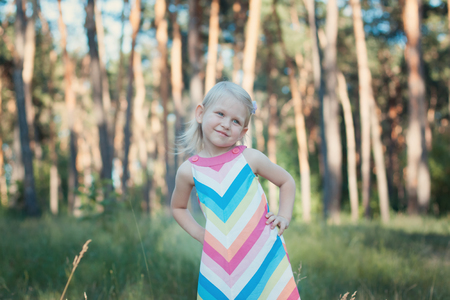 Little girl blonde in a colorful dress in the forest. She looks away and smilingの写真素材