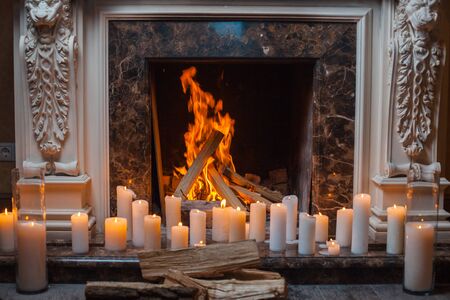 In a fireplace fire burns. Near the fireplace is a lot of burning candlesの写真素材