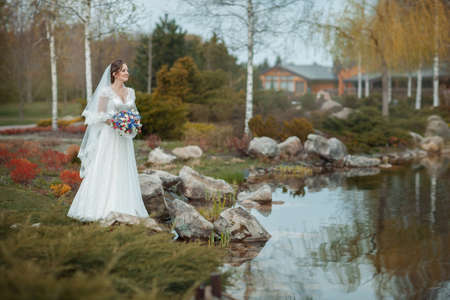 Bride standing on the shore of the pond. She is holding a bouquetの写真素材