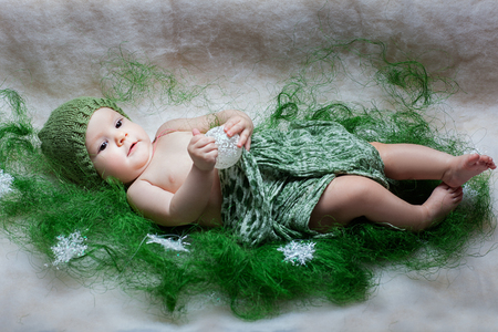 Portrait of a baby girl. She lies and holding a Christmas toy. Nearby lie snowflakesの写真素材
