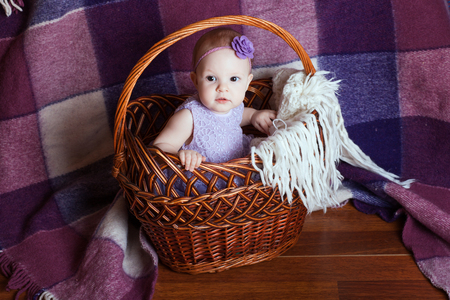 A little baby girl in a dress sits in a basketの写真素材