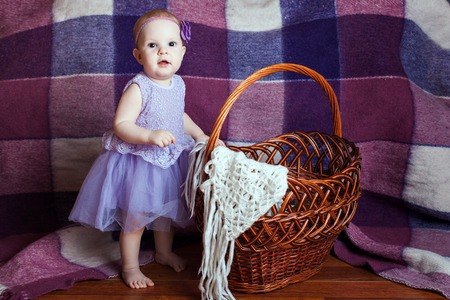 Little girl in a beautiful dress stands near a wicker basketの写真素材