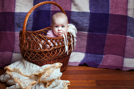 Adorable baby girl sitting in a wicker basket and showing tongueの写真素材