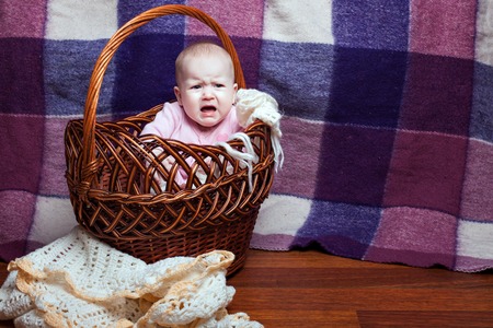 Little baby girl sitting in a basket and cryingの写真素材