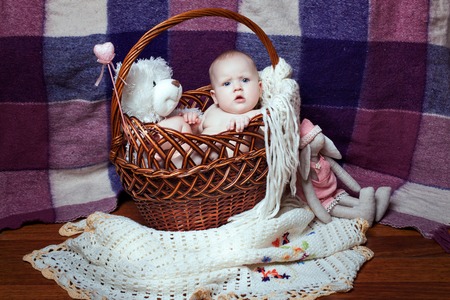 Beautiful baby girl in a wicker basket. Toy bear in a basketの写真素材