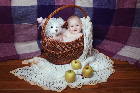 Baby girl sitting in a basket with a toy bear. Apples are close to the basketの写真素材