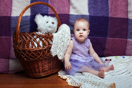 Adorable baby girl in a lilac dress sitting near wicker basketの写真素材