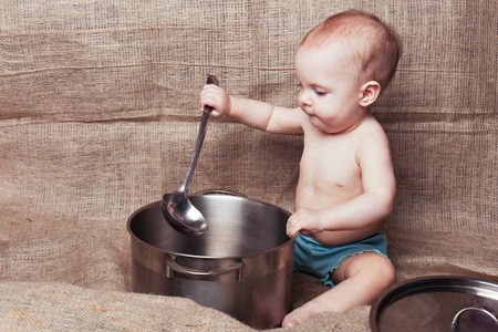 Little girl sits and plays with a pan and ladleの写真素材