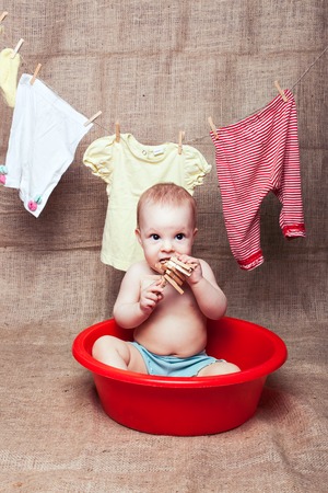 Little girl sitting in red pelvis and gnaws a wooden clothespinの写真素材