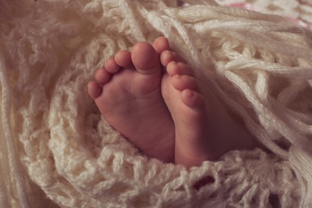 Small legs baby bundled up in a white knitted blanketの写真素材
