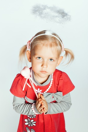Portrait of a little girl with a toy a nimbus on her head. Girl clasped her hands in prayerの写真素材