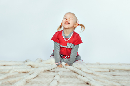 Baby blonde girl is sitting and licking on a white backgroundの写真素材