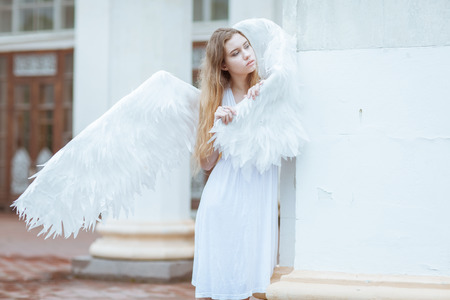Young woman with angel wings standing near a column and looking awayの写真素材