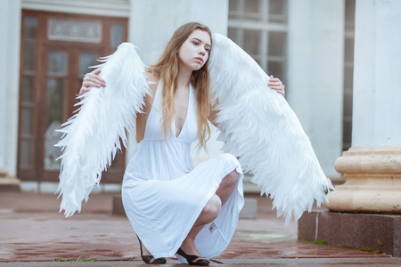 Girl angel with big white wings sitting and looking awayの写真素材