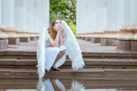 Girl angel pondered. She sits near the water and looking at the skyの写真素材