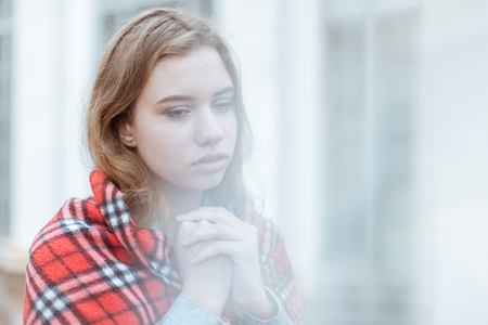 Portrait of sad beautiful young woman. She wrapped herself in a blanketの写真素材