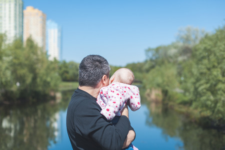 Dad and baby girl standing near the river. They stand backの写真素材