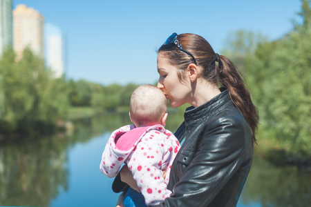 Mother and her little daughter standing near the river. Mother holding daughter in her arms and kissesの写真素材