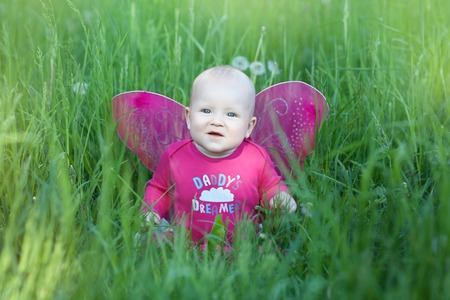 Child girl with wings sitting in the grassの写真素材