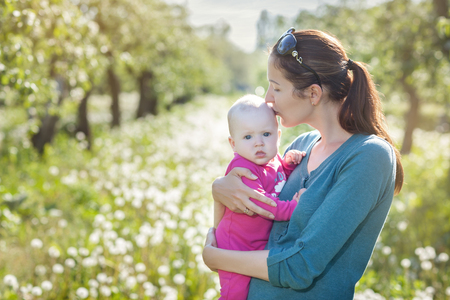 Mom and child in the garden. Mom holding the baby in his arms and kissesの写真素材