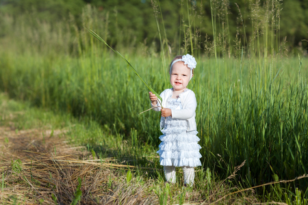 Baby girl in a white dress standing in fieldの写真素材