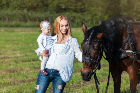 Mama and her little daughter standing in a meadow near a horseの写真素材
