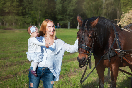 Young mother and child near a horse. Mother stroking a horse and smilingの写真素材