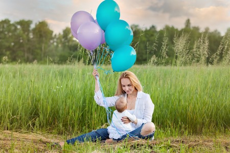 Mom sits on the grass with a child. Mom with balloonsの写真素材