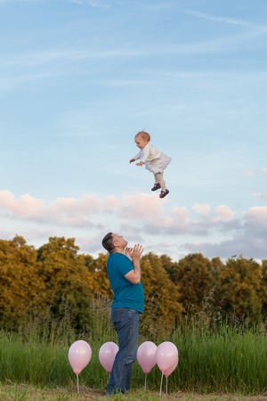 Dad and daughter in the meadow among the balloons. Dad throws daughter up highの写真素材