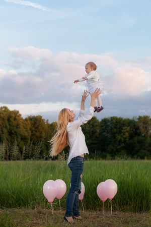Mom and daughter on the field among the balloons. Mom throws up her daughterの写真素材
