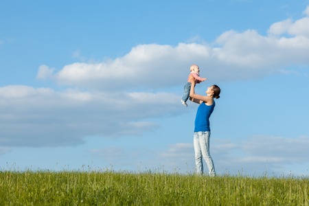 Mom and daughter on a meadow against the sky. Mom throws daughter upの写真素材