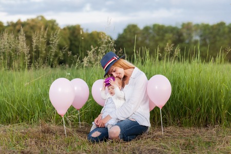 Mother and daughter sitting in a meadow. Around them balloons. Mother hugging daughterの写真素材