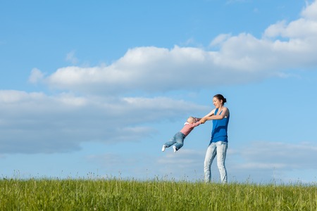 Mom and daughter on a meadow against the sky. Mom turns daughter